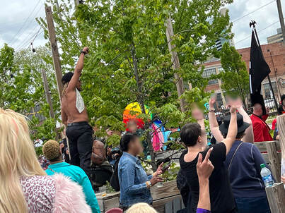 Drag King Devon Ayers stands defiantly in front of a hate group, fist raised in the air, during a performance at the Land-Grant Drag Brunch on April 29, 2023.